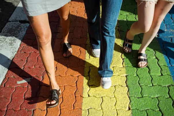 Three people walking on a rainbow crosswalk.