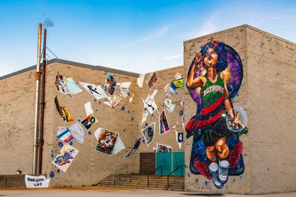 Mural depicting child wearing a dress reading Roxbury blowing bubbles and surrounded by blowing posters and books