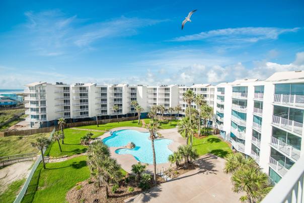 Sandcastle Resort Condominiums from above, a bird flying in the sky, and there is a pool in the middle.