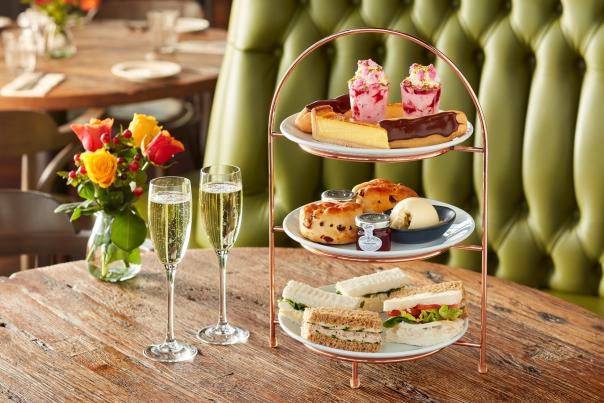Sandwiches and cakes on a platter with two glasses of prosecco.
