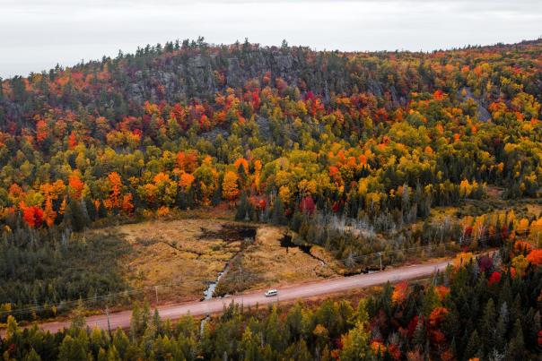 A vehicle driving on a road surrounded by vibrant fall color in the Upper Peninsula of Michigan