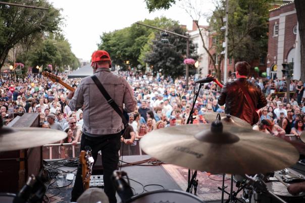 two men playing guitar on a stage with a large crowd in background