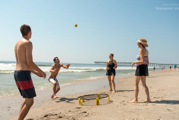 a group of four people playing a game with a small ball and a net on the beach