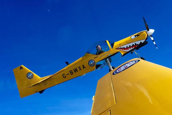a yellow stunt aeroplane in the sky with a face painted on the nose