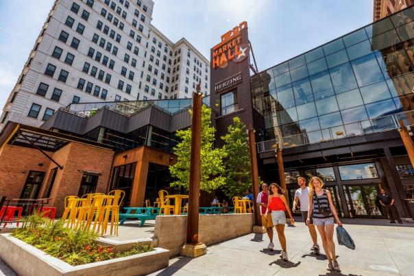 Visitors walk outside 3rd Street Market Hall in downtown Milwaukee, passing colorful outdoor seating beneath the venue’s large sign.