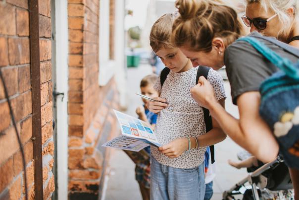 A woman and a child looking at a visitor guide in front of a brick wall