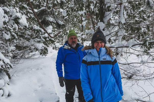 a couple smiles as they snowshoe through a snowy forest
