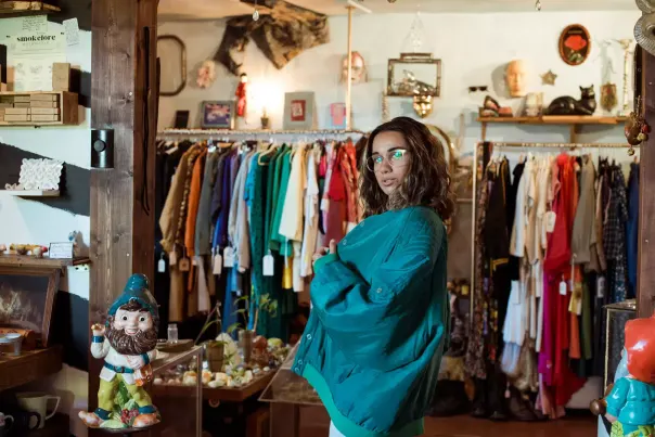 A person posing in front of a vintage store clothes rack.