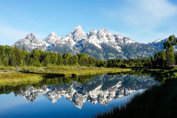 The Grand Tetons reflect against the lake from Schwabaucher Landing