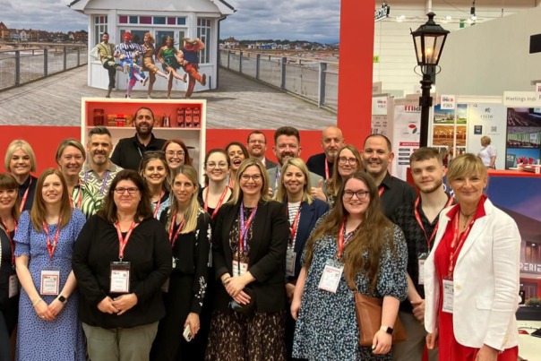 A mixed group of people standing in front of a Meet England booth at IMEX2024