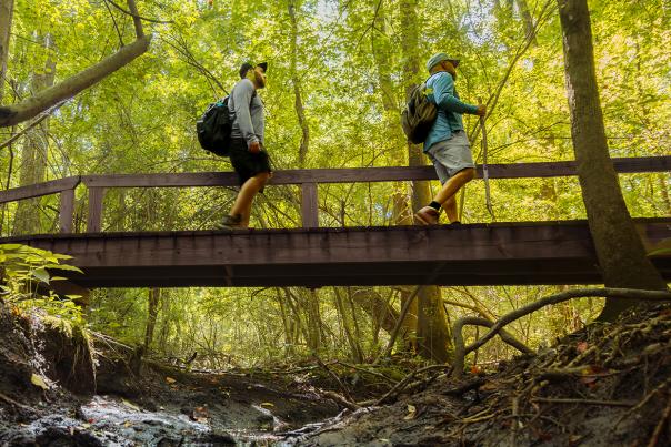 Two man cross over a bridge on a trail path in Bentonville.