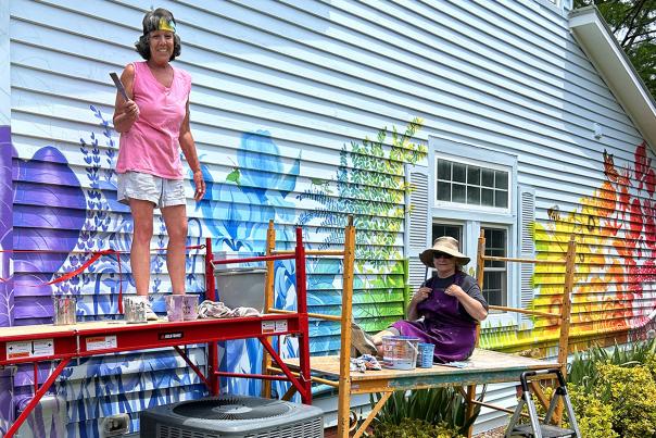 Artmosphere colorful nature mural on barn with artists posing while working.