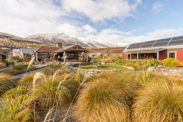 Exterior view of The Headwaters Eco Lodge, with native bush, rustic cabins and snowy mountains in the background