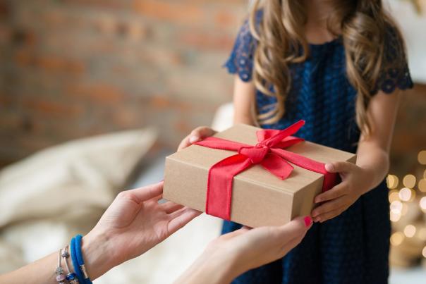 Person handing brown gift box with a red bow to a young girl