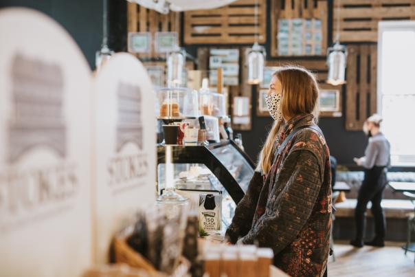 A woman stood at a counter in a coffee shop wearing a face mask
