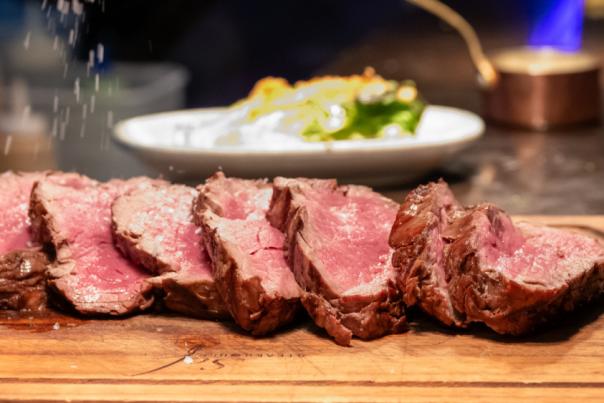 A wooden board with sliced beef steak and a gold coloured sauce jar