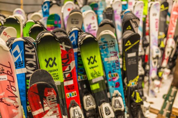 A close-up of a variety of colorful skis stacked together, showcasing different brands and designs, ideal for winter sports enthusiasts.
