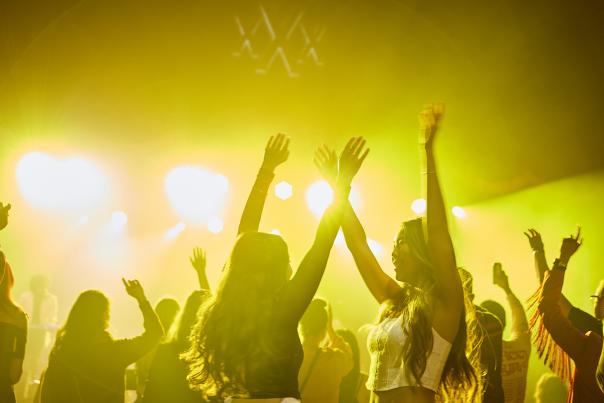People dancing with their arms in the air in yellow light