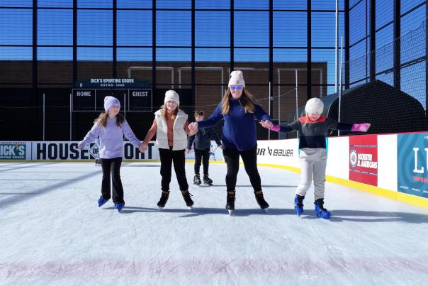 A mother and her three kids holding hands while ice skating on the outdoor rink at DICK'S House of Sport in Victor, NY