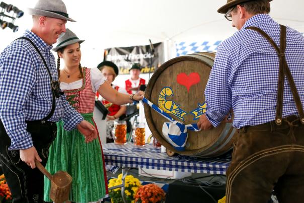 Attendees in traditional dirndl and lederhosen tap a decorated beer barrel at Oktoberfest in Lovettsville, Virginia.