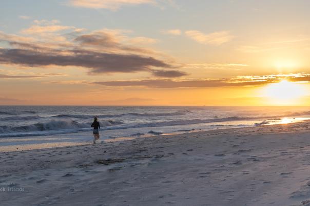 a woman running on the beach in the direction of a sunset
