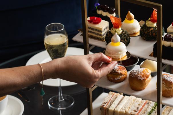Person's hand picking up cake from Afternoon tea platter with glass of champagne