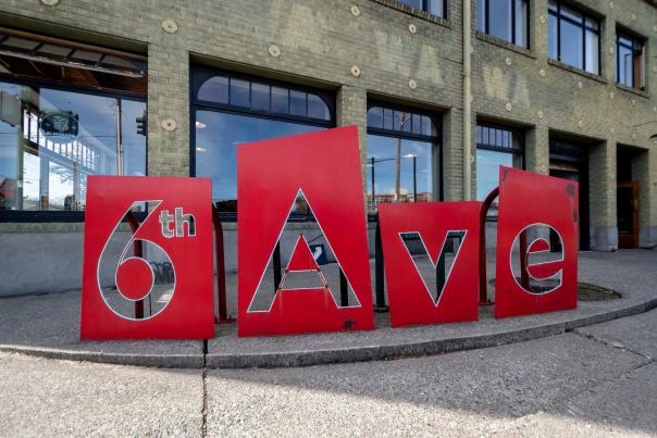 Large red panels spelling “6th Ave” on a sidewalk outside a brick building in Tacoma.
