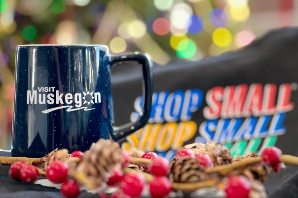 Blue mug with white Visit Muskegon log sits among holiday decor and Shop Small shopping bag