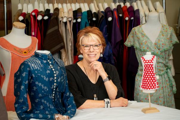 Woman with her hand raised to her chin, sits between vintage dress forms