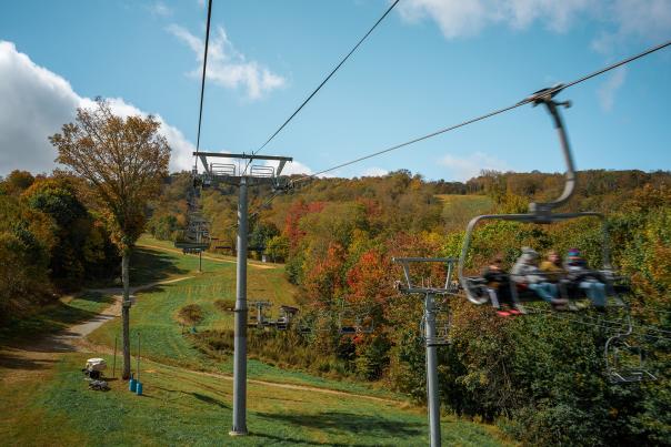 A family of four rides a ski lift in autumn.