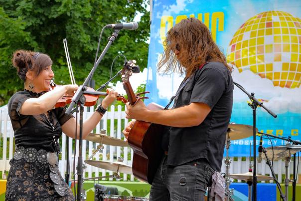 Man plays guitar and woman plays violin together during an outdoor performance.