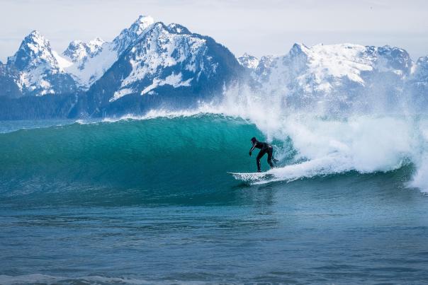 A surfer rides a wave with mountains in the background.