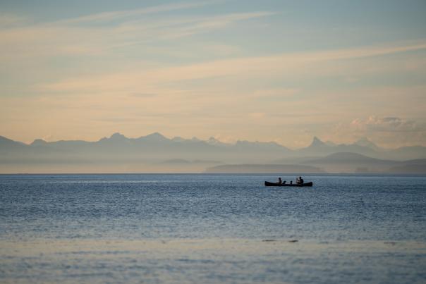 Two people kayaking on the ocean with mountains in the distance.