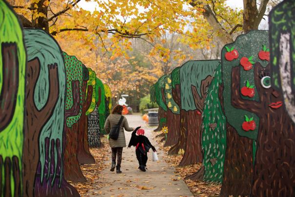 A woman and a child walk hand-in-hand down a fall path with painted fake trees on either side.