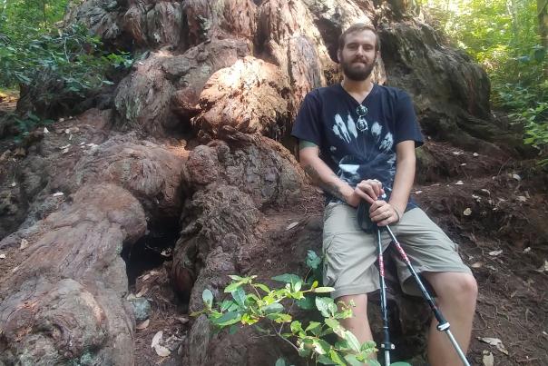 Austin posing while hiking in front of  the largest known redwood in the world, Hyperion, in Redwood National Park.