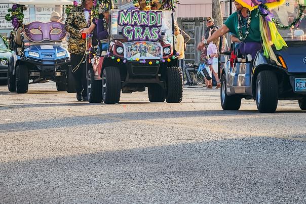 Golf carts decorated for mardi gras driving in the Port Aransas Mardi Gras Parade.