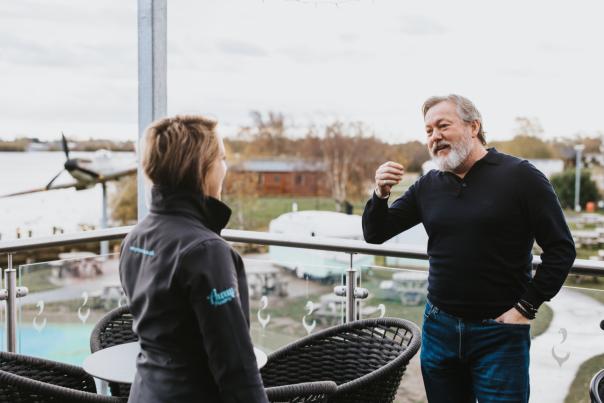 a man and a woman having a conversation on a balcony with a lake in the background