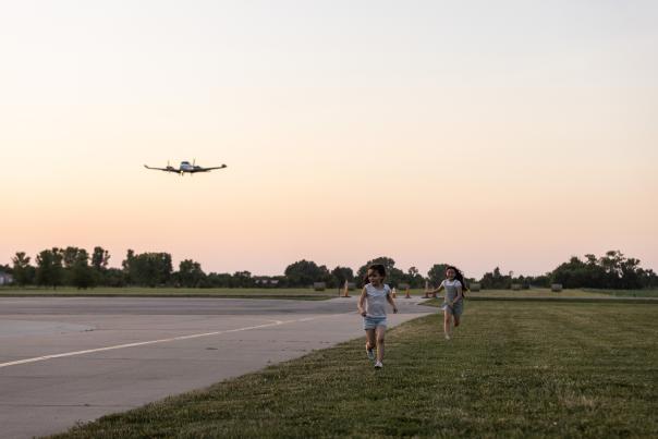 two girls running in the grass, a plane getting ready to land beside them