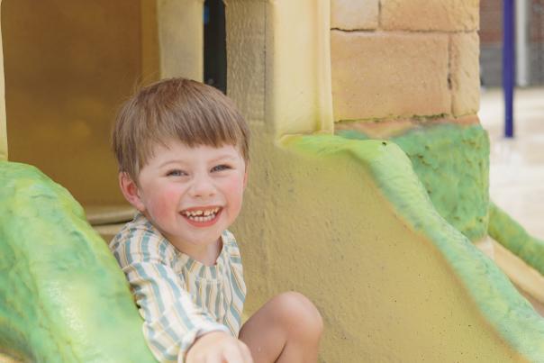 A young boy smiles as he goes down a slide at Chelsea Splash Pad.