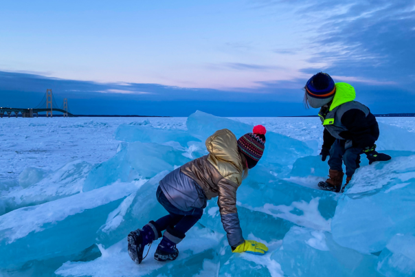 Children climbing on blue ice with the Mackinac Bridge in the background, located in the Upper Peninsula