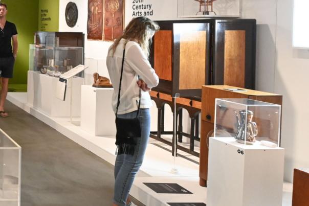 Various museum exhibits with people looking at them. A glass display case in the foreground