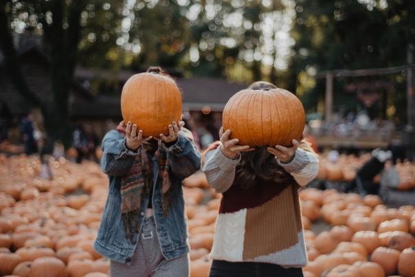 Two people holding pumpkins in front of their faces at a pumpkin patch in Vancouver, WA.