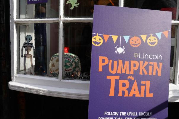 a Lincoln pumpkin trail sign in front of a window decorated with a skeleton and a pumpkin