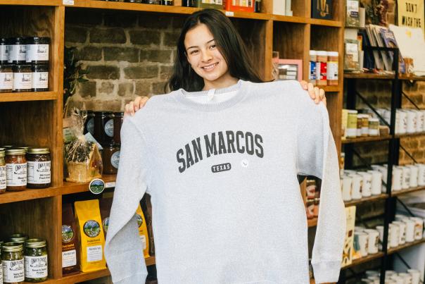 Rae Tinney poses with a San Marcos sweater at The San Market in Downtown San Marcos, Texas