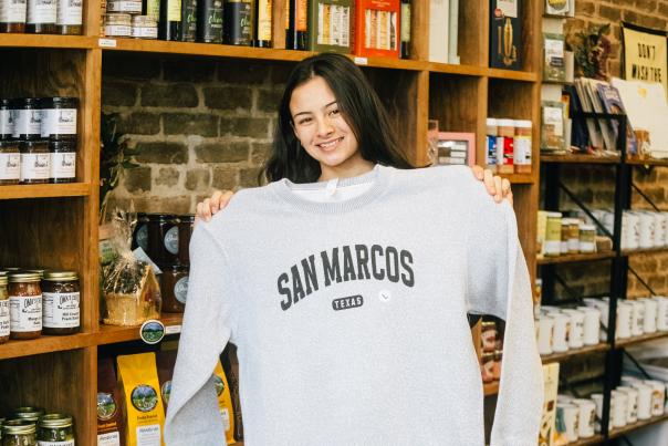 Rae Tinney poses with a San Marcos sweater at The San Market in Downtown San Marcos, Texas