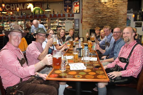 People sit a table hoisting beer steins and dressed for Ocktoberfest.