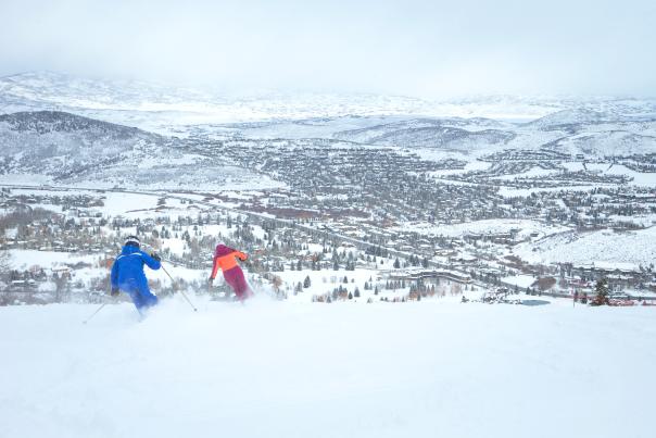 Two people skiing at Park City Mountain with a view of the town in the background