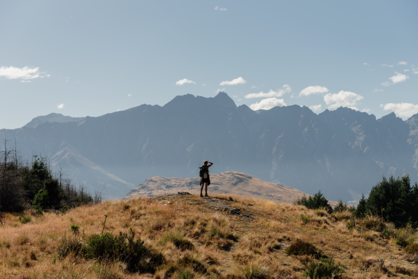 Person at the top of the Queenstown Hill summit with mountains behind them