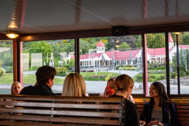 A group of people sitting on the TSS Earnslaw with a view of Walter Peak through the windows