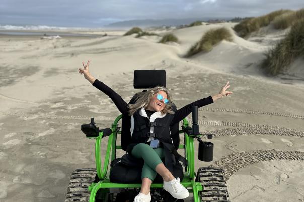 Kirstin with her arms raised in celebration in a track chair on the beach.